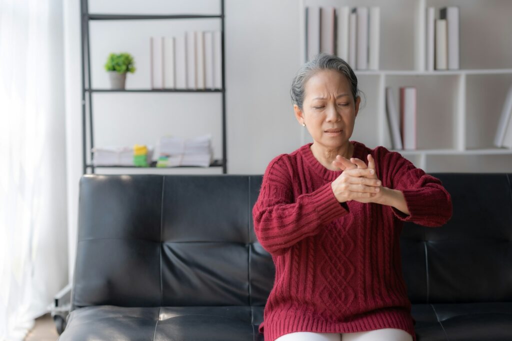 Asian old woman with body aches, leg pain, pain, arm pain, hand pain, sitting on the sofa at home.