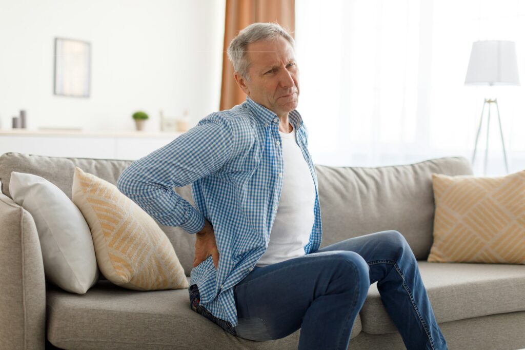 Mature man with back pain sitting on couch at home